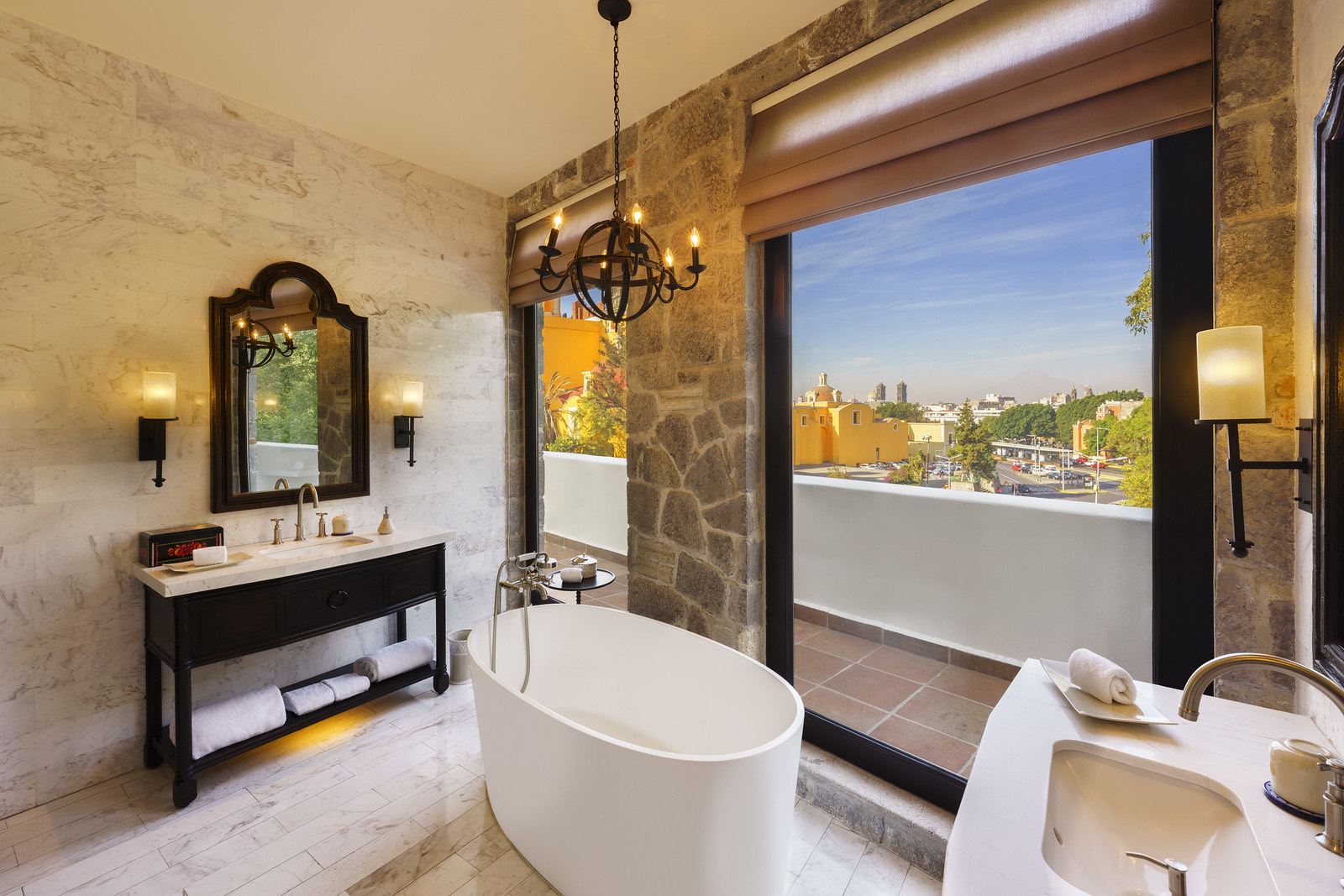 Baño con tina exenta, muros de piedra y vista a la ciudad